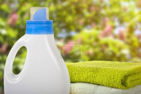 Foto de Recipiente de plástico para detergentes y toallas sobre un fondo de jardín borroso. Concepto de limpieza. - Imagen libre de derechos