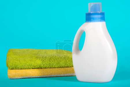 Foto de Botella de plástico blanco de detergente y toallas limpias sobre un fondo azul. - Imagen libre de derechos