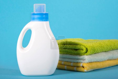 Foto de Botella de plástico blanco de detergente y toallas limpias sobre un fondo azul. - Imagen libre de derechos