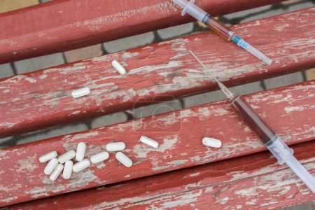 Photo for Addiction and drug abuse concept. Syringes and pills on a bench, close-up. - Royalty Free Image