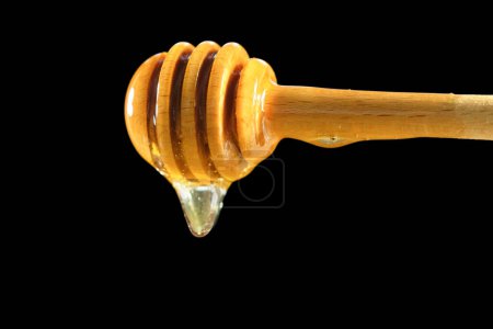 Téléchargez les photos : Louche en bois avec miel égoutté isolé sur fond noir, produits apicoles naturels biologiques. - en image libre de droit