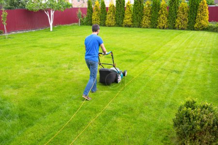 Téléchargez les photos : Un homme avec une tondeuse à gazon coupe de l'herbe verte. Un jardinier qui travaille dans le jardin. - en image libre de droit
