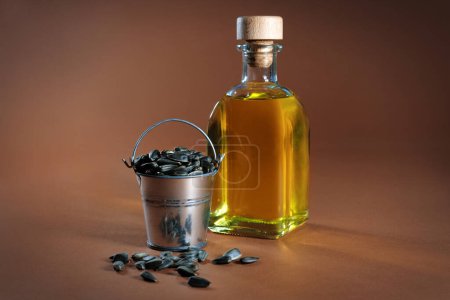 Foto de Cubo con semillas y una botella de aceite de girasol sobre un fondo marrón. - Imagen libre de derechos