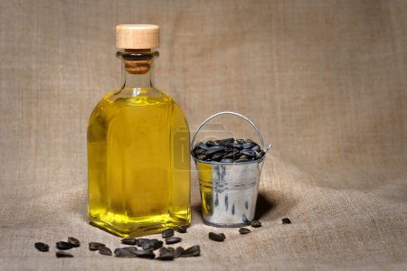Foto de Cubo con semillas y una botella de aceite de girasol sobre un fondo marrón. Granja. - Imagen libre de derechos