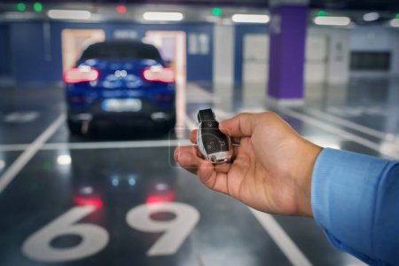Photo for Car keys in a hand of the person against the background of the car. underground parking. - Royalty Free Image