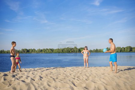 Téléchargez les photos : Une famille sur les rives de la rivière jouant au volley-ball par une journée ensoleillée d'été. Mode de vie sain. - en image libre de droit