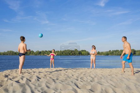 Téléchargez les photos : Une famille au bord de la rivière jouant avec une balle. Saison estivale. Style de vie sportif. - en image libre de droit