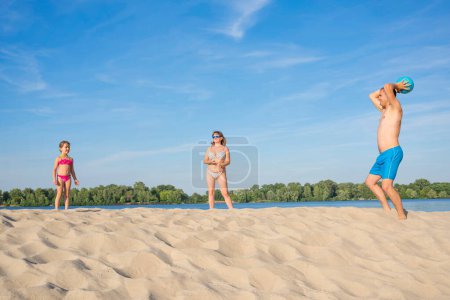 Téléchargez les photos : La famille joue avec la balle bleue sur la rive de la rivière. Le concept est un mode de vie sain. - en image libre de droit
