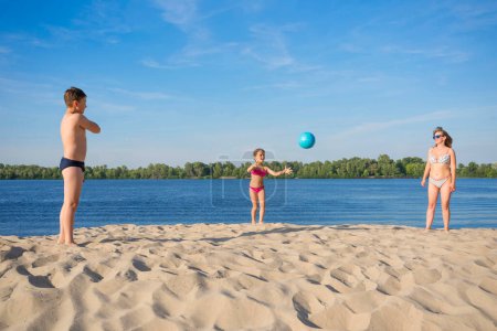 Téléchargez les photos : La famille joue au volley-ball sur le sable, par une journée ensoleillée et lumineuse. Jeux de sport. - en image libre de droit