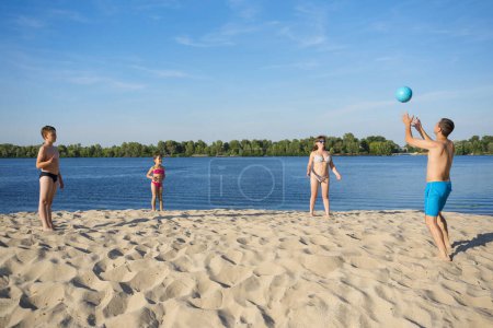 Téléchargez les photos : La famille joue au beach-volley sur la rive sablonneuse de la rivière. Un mode de vie sain. - en image libre de droit