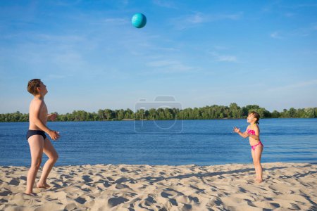 Téléchargez les photos : Enfants heureux jouant avec une balle sur la plage. Les enfants s'amusent pendant les vacances d'été. - en image libre de droit