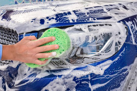 Téléchargez les photos : Un homme lave une voiture bleue savonneuse avec une éponge verte. - en image libre de droit