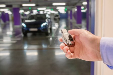 Photo for Car keys in a hand of the against the background of the car on underground parking. Closeup - Royalty Free Image