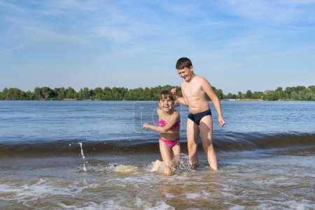 Foto de Hermano y hermana huyendo de las olas del río en la playa. Los niños juegan en el agua. Vacaciones de verano - Imagen libre de derechos
