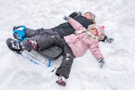 Téléchargez les photos : Un garçon et une fille heureux couchés ensemble dans la neige, faisant des anges de la neige. - en image libre de droit