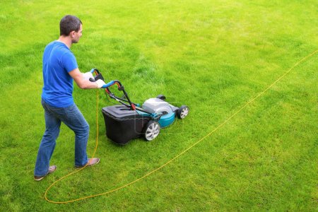 Téléchargez les photos : Jardinier dans le jardin tonds l'herbe avec une tondeuse à gazon. Vue latérale. - en image libre de droit