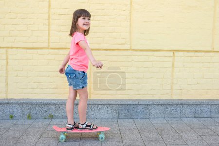 Téléchargez les photos : Jolie fille est engagée dans une planche à roulettes sur un fond de mur jaune. Style de vie sportif. - en image libre de droit
