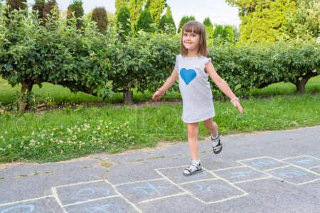 Photo for Cute little girl is playing in the park on the pavement. Childrens games in the open air. - Royalty Free Image