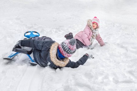 Téléchargez les photos : Un garçon et une fille heureux de s'amuser ensemble, couchés dans la neige. - en image libre de droit