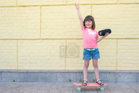 Téléchargez les photos : Petite fille avec un skateboard et écoute de la musique en plein air. Mode de vie actif. - en image libre de droit