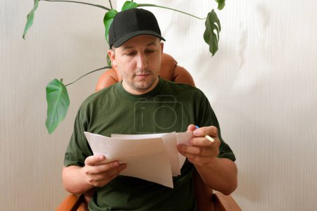 Foto de Un joven soldado que sufre de trastorno de estrés postraumático en la oficina de un psicólogo con documentos en sus manos. Consecuencias de la guerra. El concepto de guerra, trastorno mental - Imagen libre de derechos
