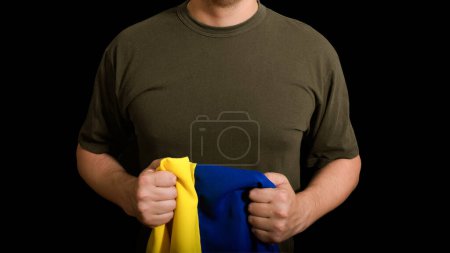 Photo for Ukraine flag in the hands of a military man on a black background. Cropped view - Royalty Free Image