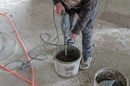 Téléchargez les photos : Travailleur mélangeant du mortier avec un mélangeur électrique. - en image libre de droit