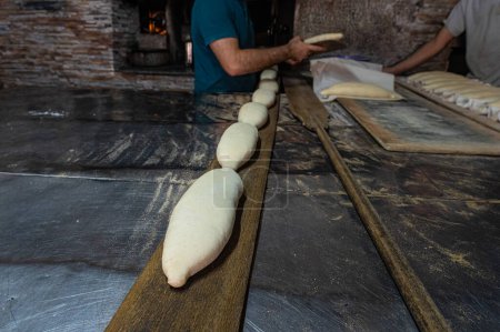 Photo for The baker putting the bread dough into the oven. Turkish bread production process. - Royalty Free Image