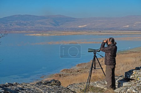 A man with binoculars bird watching on the lake.