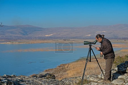 Un hombre observando aves en un lago con un telescopio.