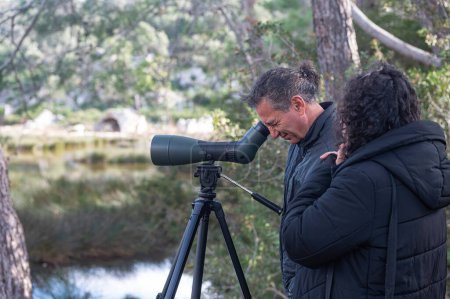 Ein Mann und eine Frau beobachten mit dem Teleskop einen Vogel im See.