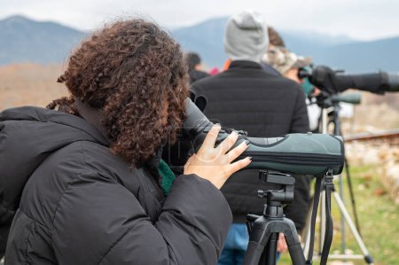 Woman birdwatching with a telescope by the lake in cold weather.