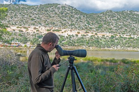 Un hombre observando aves en un lago con un telescopio.