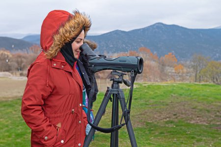 Junges Mädchen im roten Mantel beobachtet Vogelbeobachtung mit dem Teleskop am See.