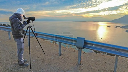 A man birdwatching with a telescope at sunrise. Lake Egirdir in Turkey.