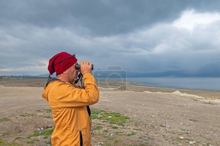 A man birdwatching with binoculars on a lake.