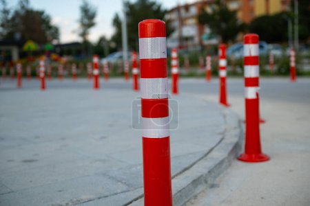 Orangefarbener Verkehrskegel, Parken verboten. Rote Plastikbarriere. Reihe roter und weißer Ampelmasten auf der Straße. Eine Barriere aus Kunststoffsäulen mit reflektierendem Pigment auf einer asphaltierten Straße. Gefahrenkonzept.