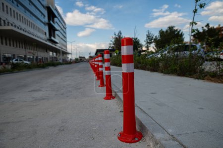 Orangefarbener Verkehrskegel, Parken verboten. Rote Plastikbarriere. Reihe roter und weißer Ampelmasten auf der Straße. Eine Barriere aus Kunststoffsäulen mit reflektierendem Pigment auf einer asphaltierten Straße. Gefahrenkonzept.