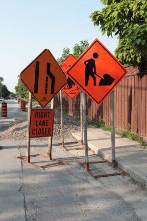 Photo for Three road construction signs on wood stands next to sidewalk with one that says right lane closed, another with a person digging shoveling, and all orange with black print - portrait shot - Royalty Free Image
