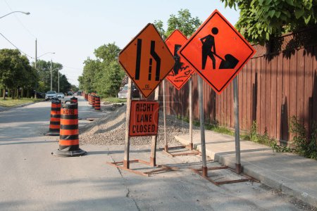 Photo for Three road construction signs on wood stands next to sidewalk with one that says right lane closed, another with a person digging shoveling, and all orange with black print - Royalty Free Image