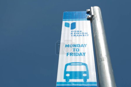 Téléchargez les photos : York region transit lundi au vendredi panneau de signalisation de bus cadre à droite, impression bleue sur fond avec ciel clair derrière contre poteau métallique argenté - en image libre de droit