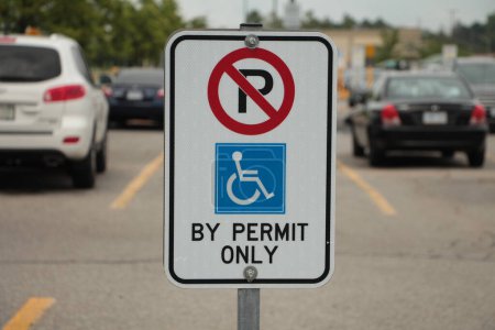 Photo for Handicap no parking sign with handicap logo and by permit only writing text caption in parking lot with blurred parked cards behind, blue red white yellow - Royalty Free Image