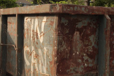 Photo for Dumpster that says tin can on side in capital letters, old beat up rusted worn faded, with sun shining on writing, close shot - Royalty Free Image
