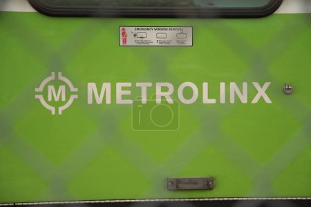 Téléchargez les photos : Logo metrolinx en écriture blanche sur le côté du train vert stationné à la gare tourné à travers la clôture - en image libre de droit