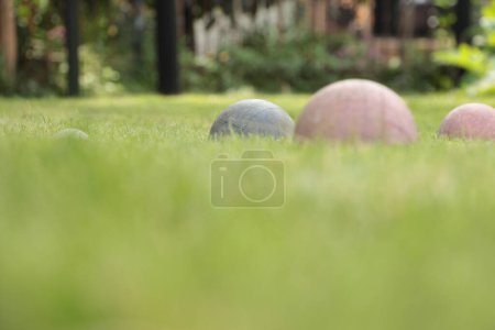 Photo for Italian game bocce, old worn set of balls with one green and two red in shot screen right with the white ball screen left, shot from low angle with blurred grass in foreground - Royalty Free Image