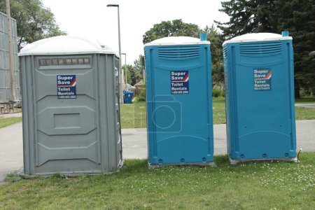 Photo for Three porta portable potties next to each other on grass, one gray and two blue, super save toilet rentals stickers on them, pavement and grass behind - Royalty Free Image