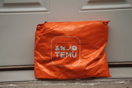 Foto de Paquete del bolso del rectángulo naranja temu con el logotipo en él entrega entregada apoyada contra la puerta blanca, primer plano - Imagen libre de derechos