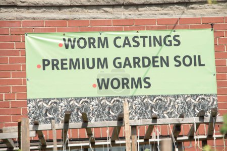 Photo for Worm castings premium garden soil worms sign in black writing on yellow background against storefront brick wall - Royalty Free Image