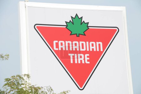 Photo for Canadian tire logo store sign by road save up to 75 percent on select items with tree in front, red triangle with green maple leaf on white background with black writing, close up on angle - Royalty Free Image