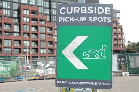 curbside pick up spots sign with arrow and illustration of person going in their car trunk, do not block accessible parking, green gray white